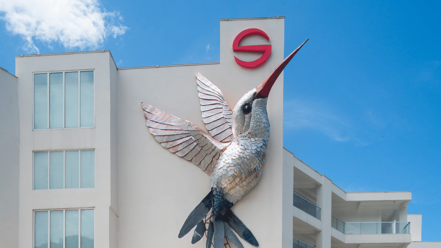 Modern hotel building with a large hummingbird mural on the facade, set against a bright blue sky, creating a striking and artistic exterior view.