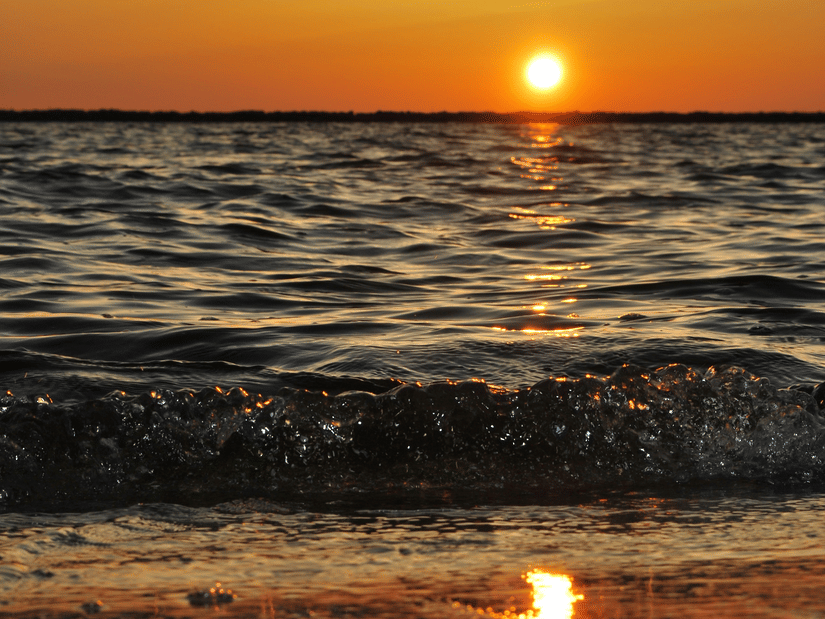 A wave of water hitting the shore of a beach during the golden hour.