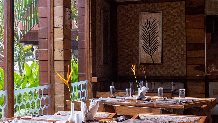 A spacious dining area at Ocean Prime with wooden tables and chairs, set in a modern wooden room. The decor is minimalist, with large windows offering a glimpse of the outside greenery - Coral Reef Resort & Spa, Havelock