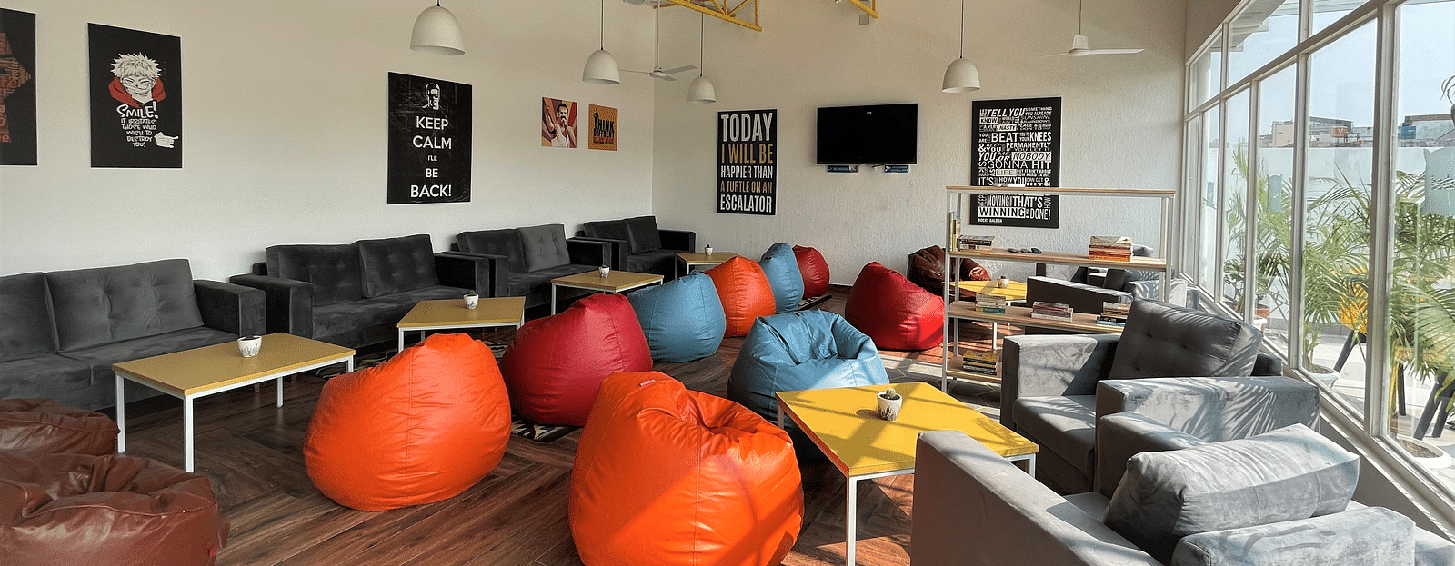 An image of a lounge area featuring sofas and bean bags for relaxation, coffee tables, and a bookshelf stocked with a selection of books to read.