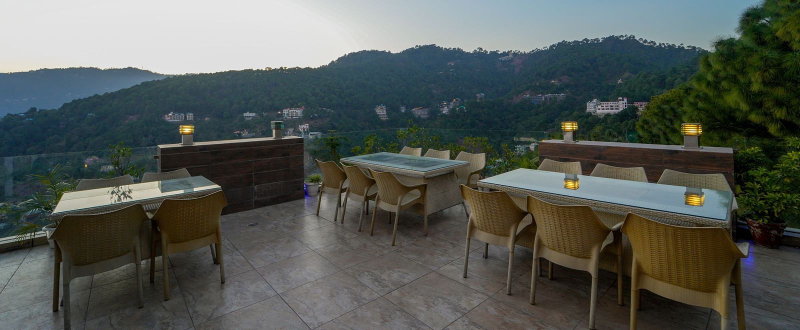 A shot taken from an angle of the terrace-top dining area with chairs and tables with the backdrop of the mountains - DLS Whispering Winds