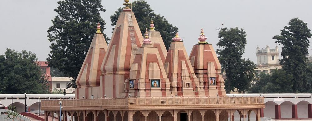 A Hindu temple with multiple domes and a large pond in front, surrounded by trees.