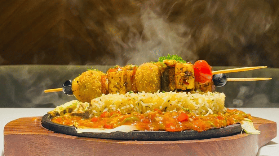 Sizzler at The Citrine, Bangalore, on a wooden platter with cottage cheese shashlik skewers, herbed rice and tomato gravy releasing steam.
