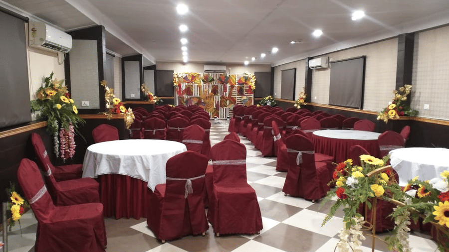 Spacious banquet hall with maroon seating, round tables, and floral centrepieces at Central Courtyard Boutique Hotel.