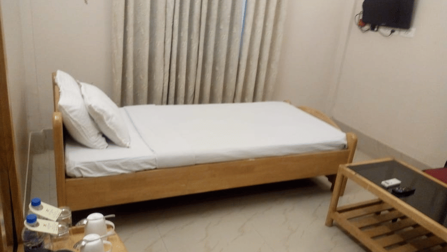 A room at Lake Side Resort Neermahal, featuring a single bed, bedspreads, a pillow, and a table.