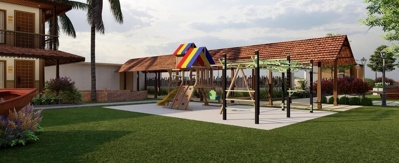 A grassy outdoor area with playground equipment and a building with a brown roof in the background, surrounded by trees and foliage.