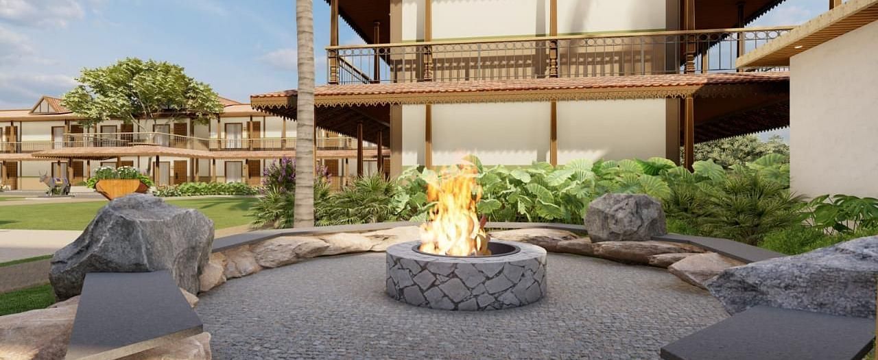 A modern building with wooden accents, an outdoor seating area with a fire pit, and lush landscaping, suggesting a resort or residential complex.