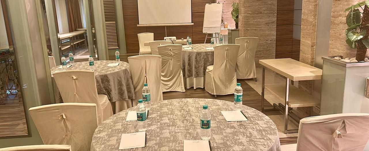  Round banquet tables with silver covers and chairs, ample seating area, projector and wooden flooring at Mirage Hotel, Mumbai.
