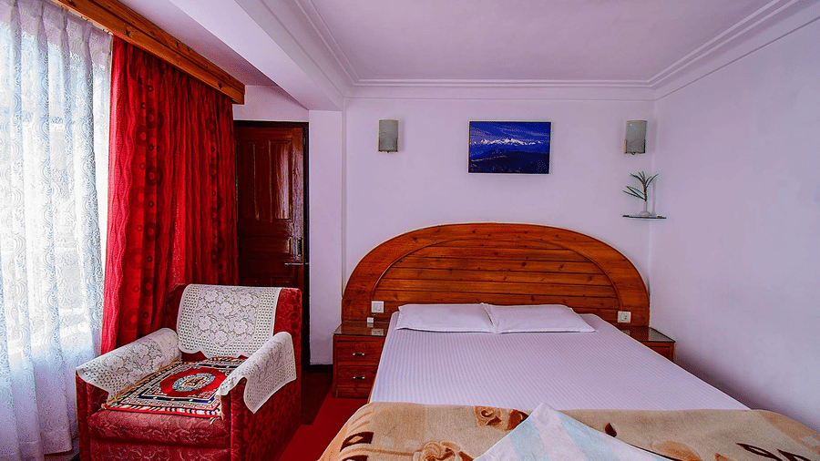 Close-up view of a double bed with a wooden headboard, red curtains, and 2 framed pictures on the wall at Hotel Dolphin Darjeeling.