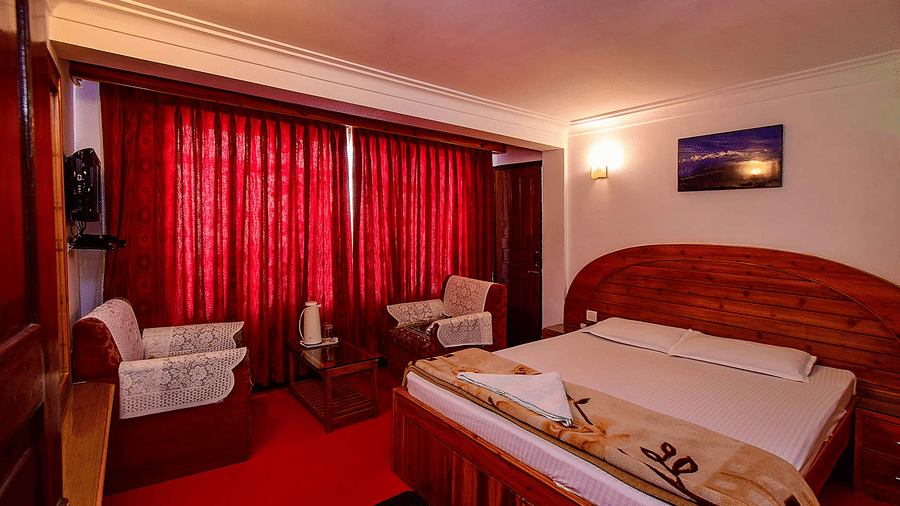 Room with a double bed, red carpet, and red curtains, lit by ceiling and bedside lamps creating a warm ambience at Hotel Dolphin Darjeeling.
