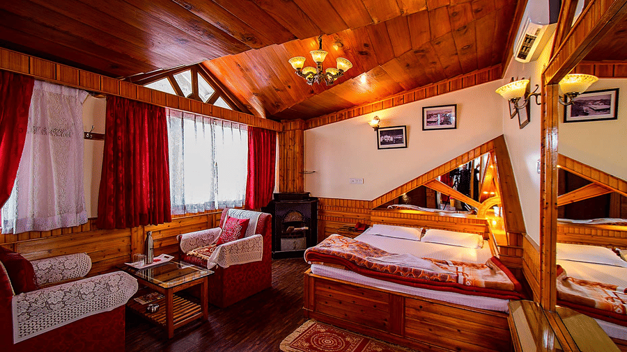 Hotel room with a wooden ceiling, double bed, red and white seating area, and wall mirrors reflecting the room at Hotel Dolphin Darjeeling.