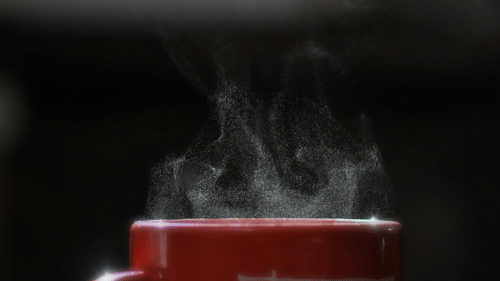 A close up shot of the steam coming out of a red cup with a hot beverage inside it.