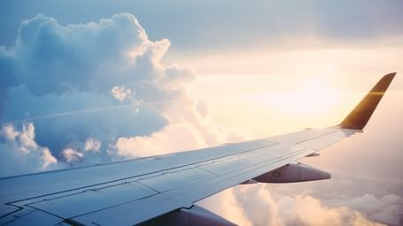 An aircraft wing slices through sunlit skies above cottony clouds.