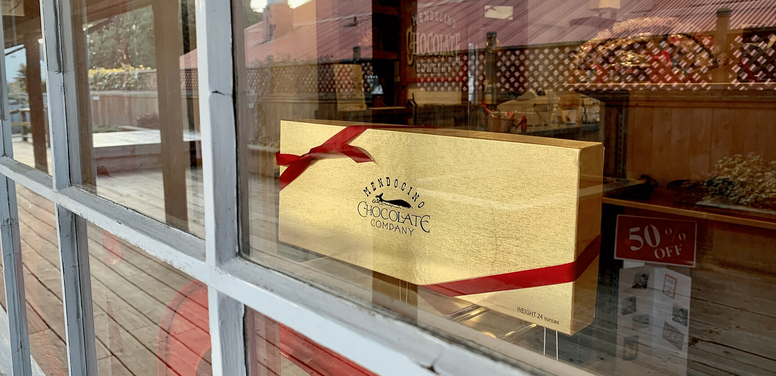 An image of a chocolate box packed with ribbons which can be seen from the glass window