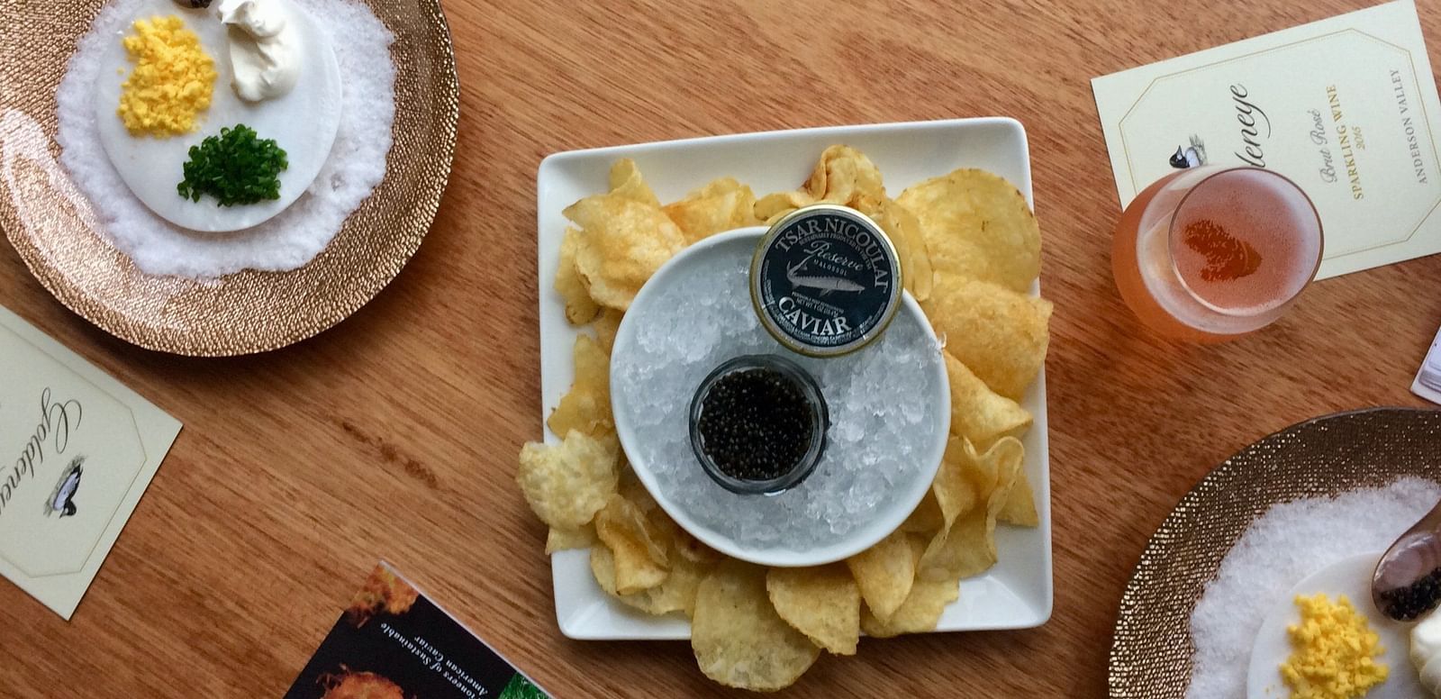 An overhead view of a caviar platter with chips and garnishes, elegantly presented on a wooden table.
