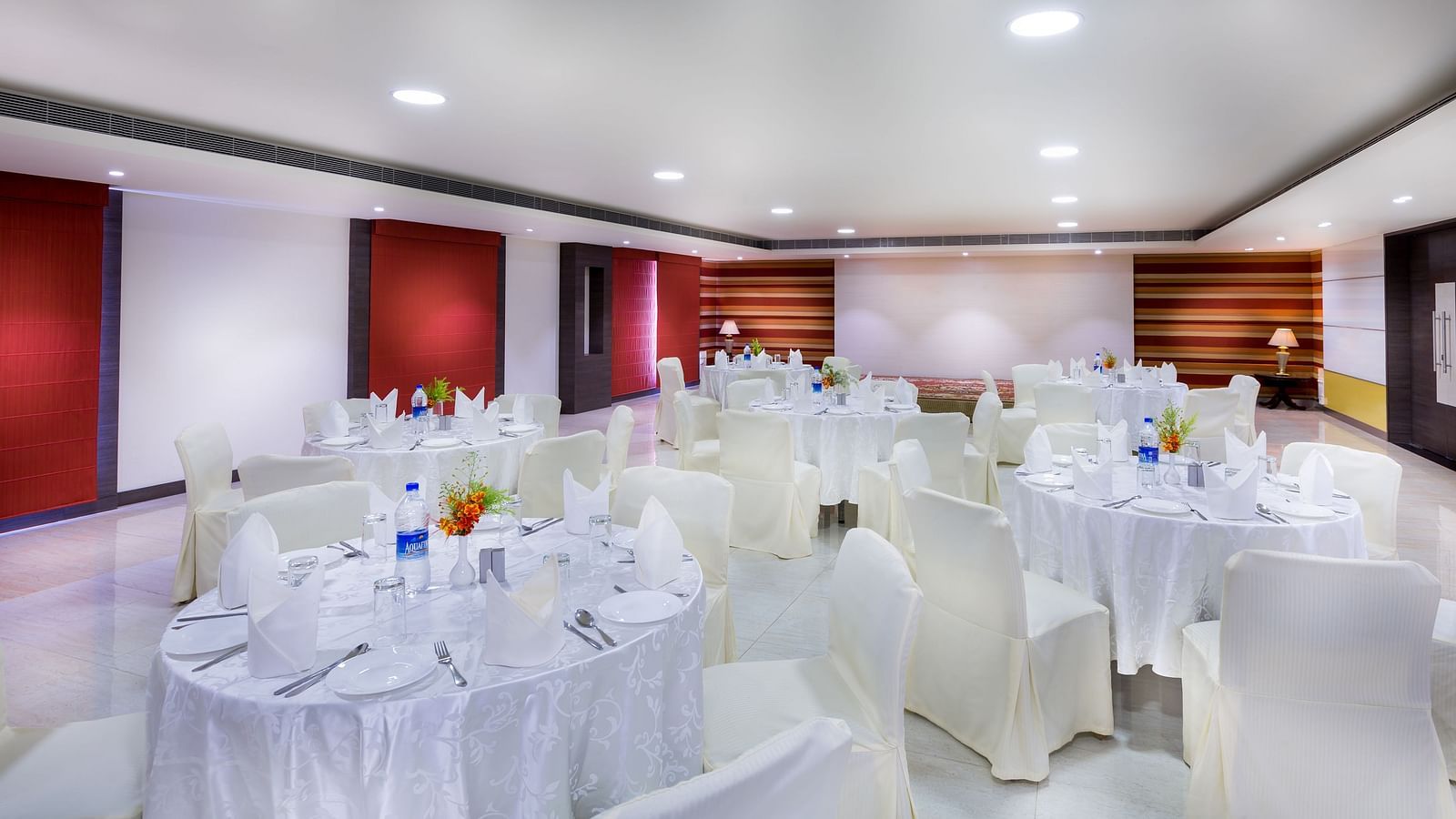 Interiors of a event hall with white chairs and tables at Regency Tiruttani by GRT Hotels.