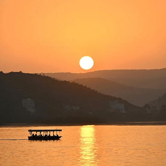 A serene sunset scene over Lake Pichola in Udaipur, with a small boat silhouetted against the horizon, a perfect way to experience the magic of Udaipur sightseeing.