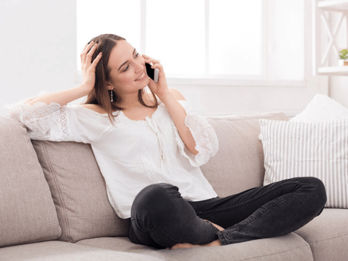 A woman smiling during a phone call on sofa with her one hand on her head at YO1 Longevity & Health Resorts