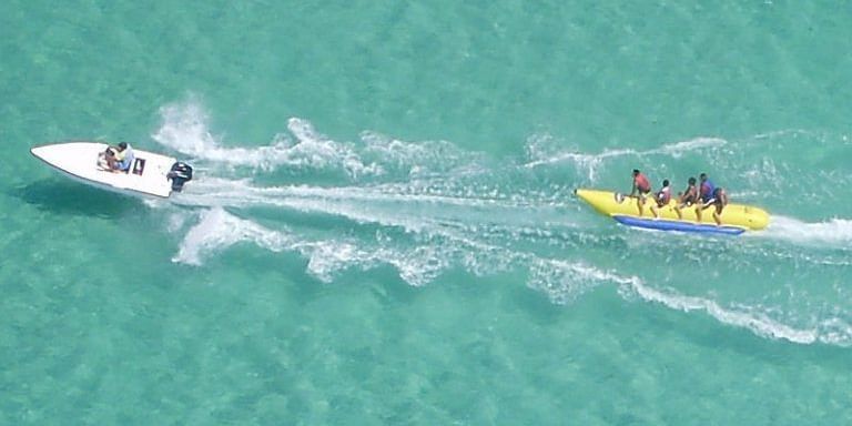 Excited riders on a banana boat whipped by a speedboat.