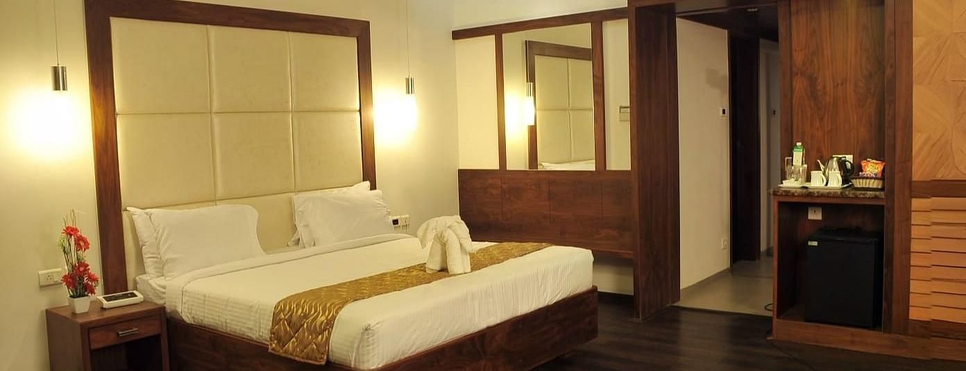 A room with a queen size bed, two side tables, wooden flooring, two mirrors, hanging lights, and a counter with bottles and appliances at Dhanalakshmi Srinivasan Hotels, Perambalur.