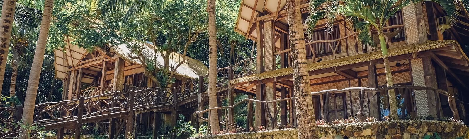 Wooden cottage-style buildings among tall palm trees at Flower Island Resort.