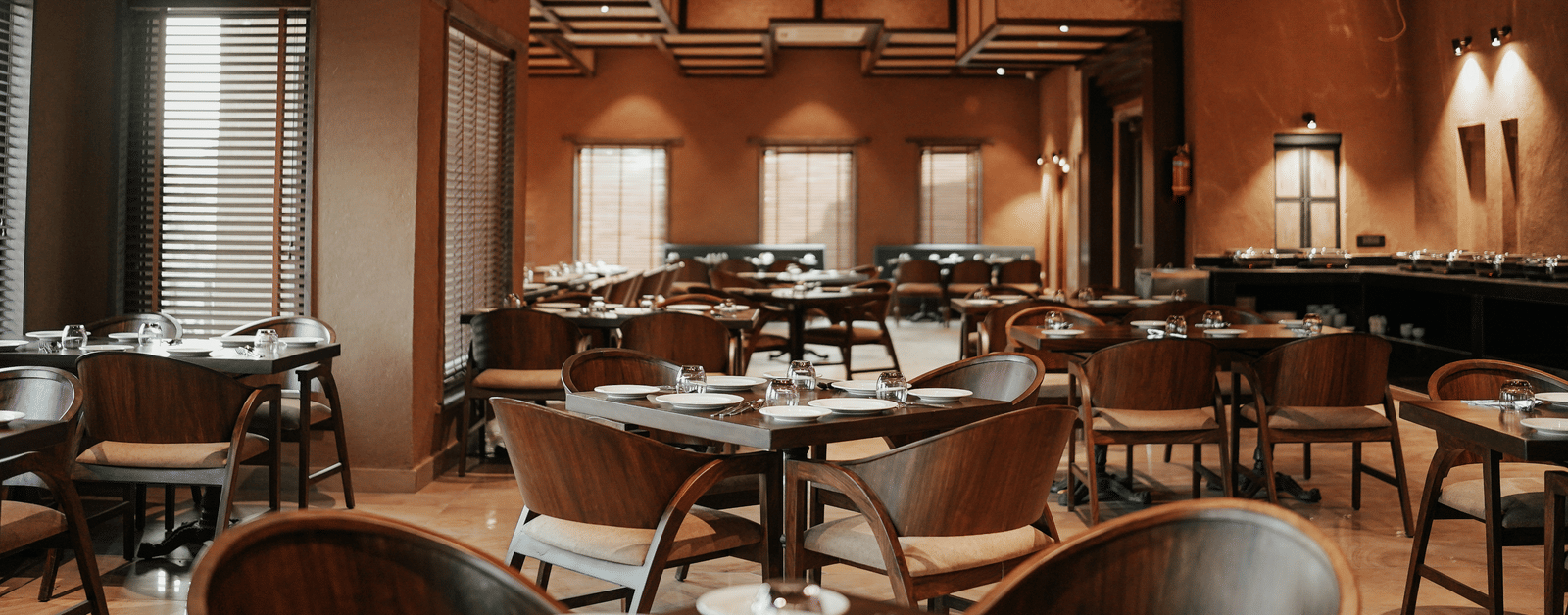 A spacious restaurant hall at Aamaghati Wildlife Resort with wooden ceilings, soft lighting, and neatly arranged tables offering guests a refined dining atmosphere.