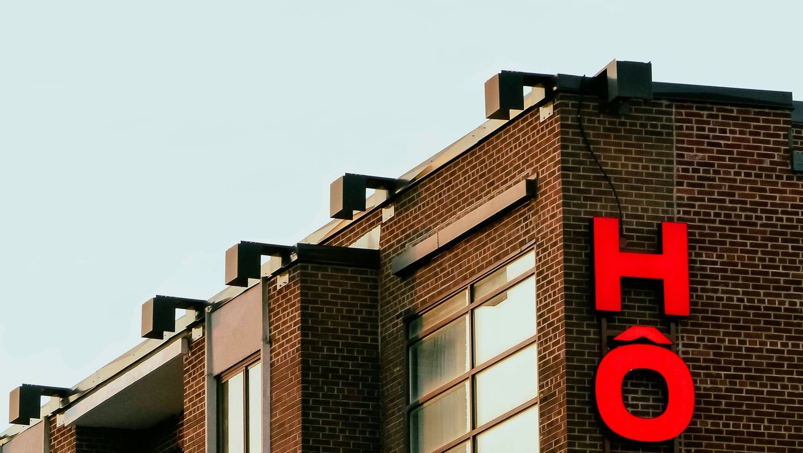 Close-up of the upper floors of an older, dark brick building with a vertical, bright red neon sign spelling out the word 'HOTEL'.