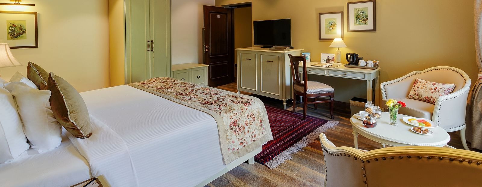 An image featuring a cosy room with decors, king size bed, ceiling designs and framed pictures seen near the flat screen TV - The Naini Retreat