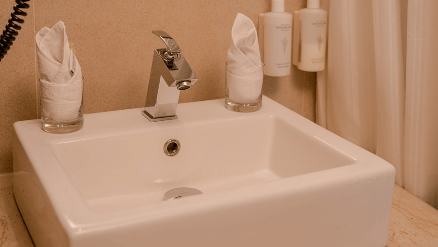 A bathroom features a square white washbasin, a wall mirror, and 2 white rolled towels on a counter at Tiara by MPS.