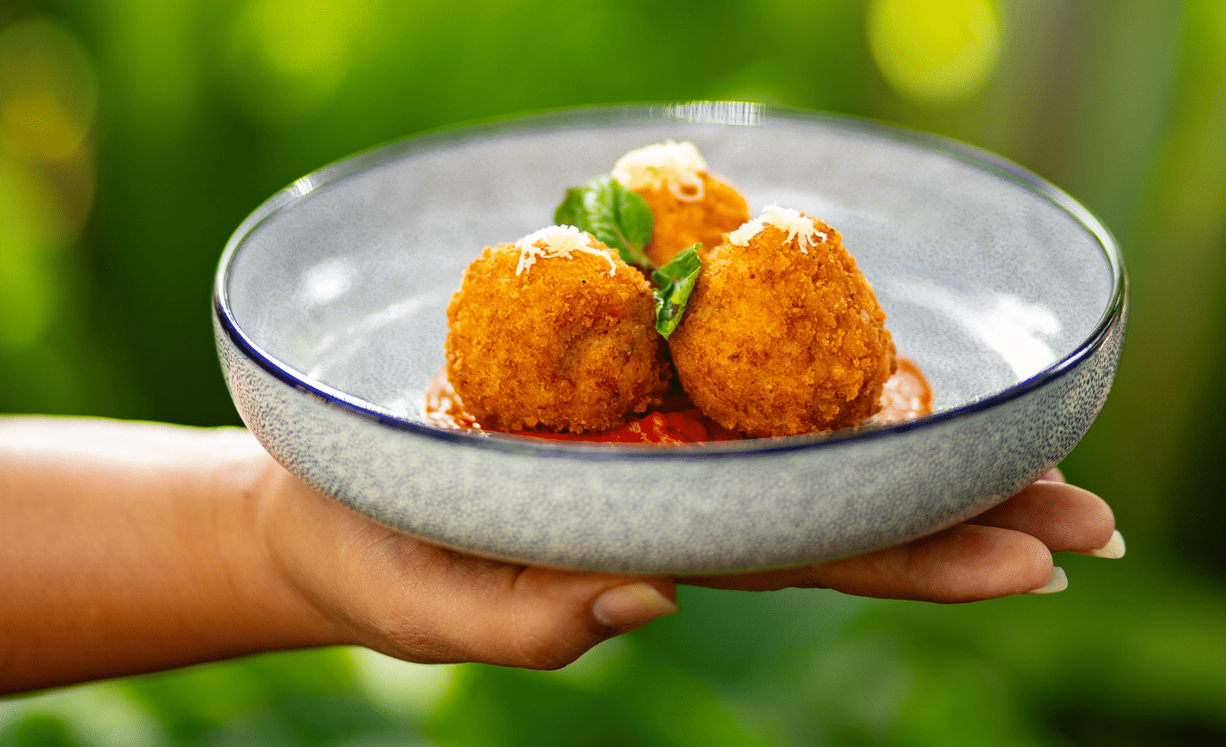 A person holds a plate with three fried, golden-brown appetisers on a bed of red sauce at Stanley Revelation.