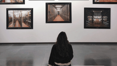a girl sitting on a bench looking at the paintings hung inside a museum