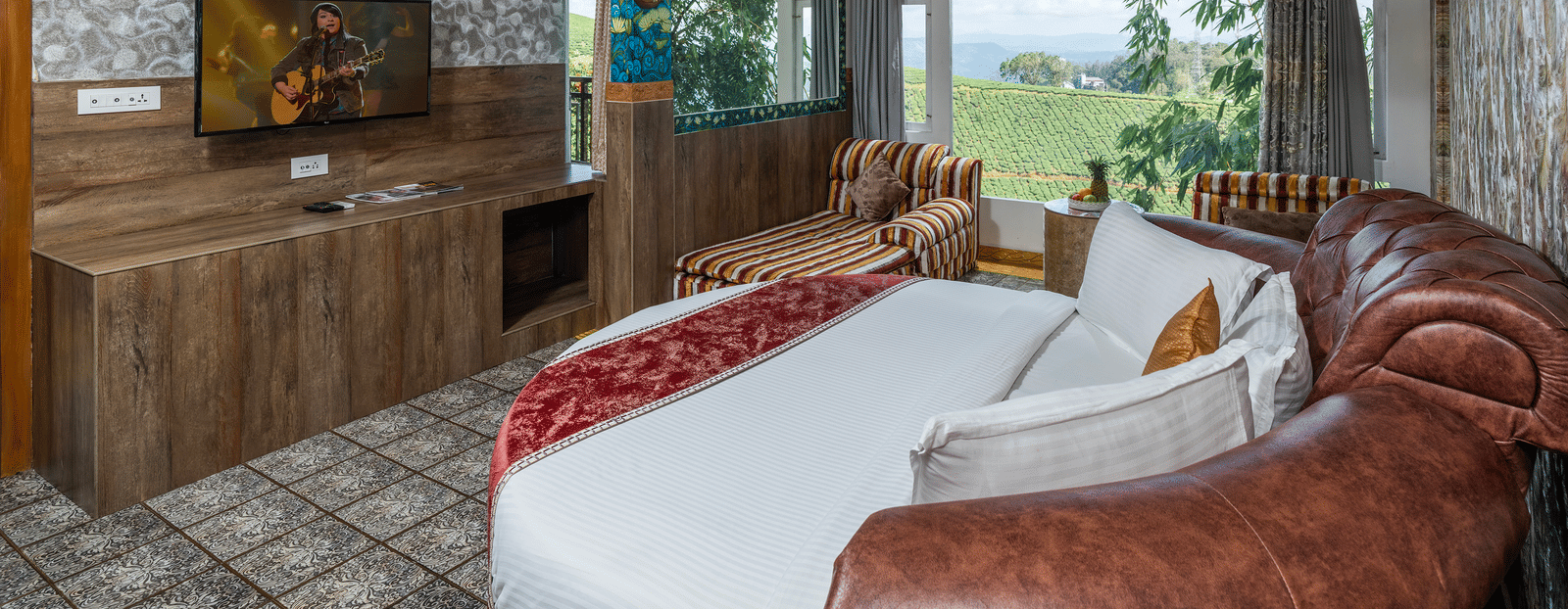 A bedroom in Family Jacuzzi Room in Parakkat Nature Hotel and Resorts, Munnar, featuring a round bed, a flat-screen TV, a ceiling fan, and an opening to a private balcony.