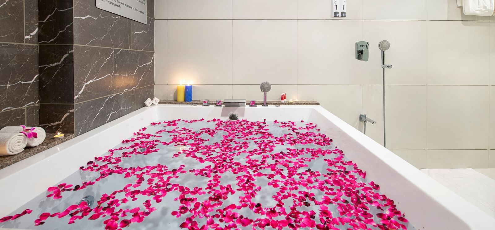 A luxurious bathtub filled with pink flower petals in a bathroom - SK Lords Inn Ahmedabad