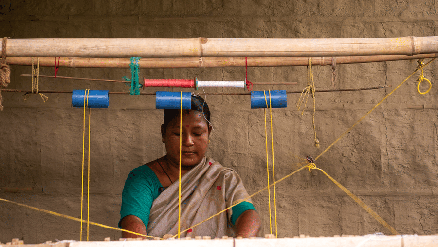 A local woman working at a traditional wooden weaving loom inside a dimly lit room.
