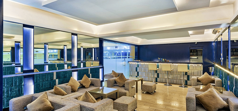 An indoor seating area with light brown sofas and blue panels at Grande Bay Resort & Spa, Mamallapuram.