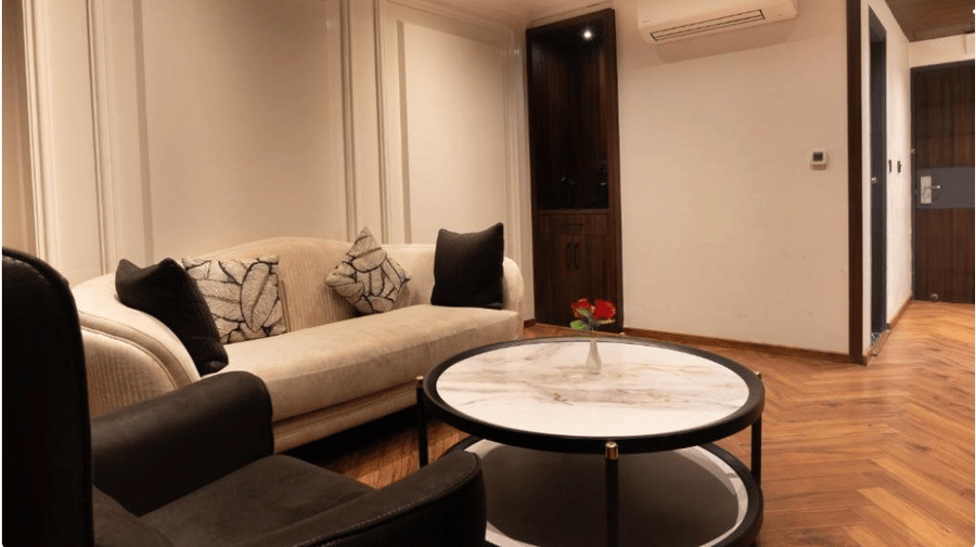 A lounge area with a sofa, an armchair, and a marble-top table next to an open doorway | Lawrence Solitaire Resort, Nainital