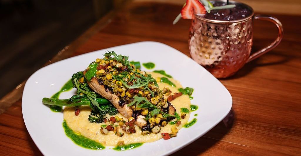 A white plate featuring a pasta dish at Shaver Lake Village Hotel with greens, nuts, and a drizzle of sauce.