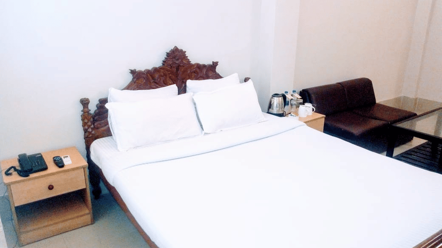 Deluxe room at Lake Side Resort Neermahal, featuring a single bed. bedspreads, pillows, a sofa, and a window covered in curtain.