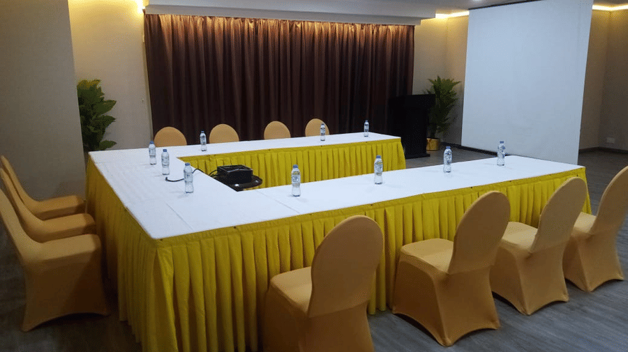 A U-shaped meeting table with yellow skirting and chairs is set up in a conference room with a projector screen - Al Manar Grand Hotel Apartment, Bur Dubai