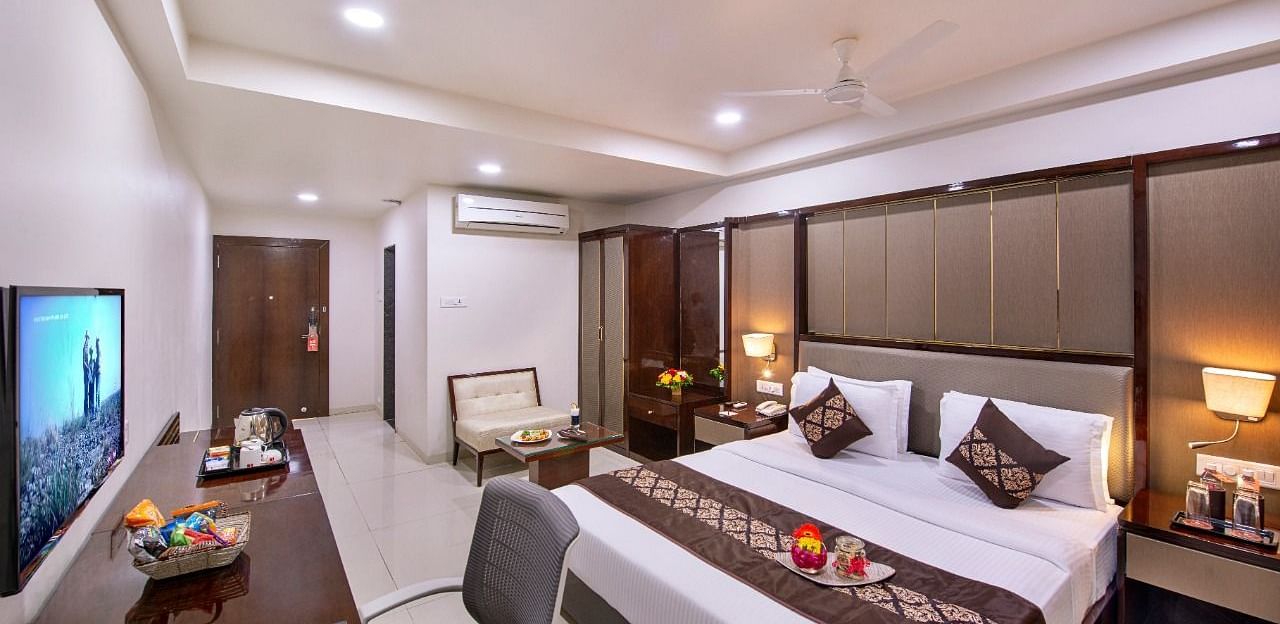 A comfortable hotel room at Lords Inn Porbandar, offers a king size bed, a seating area, a television, and warm lighting.