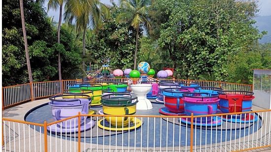 A tea cup ride with brightly colored cups and saucers against a background of lush greenery and a large rotating globe in the center of the attraction.
