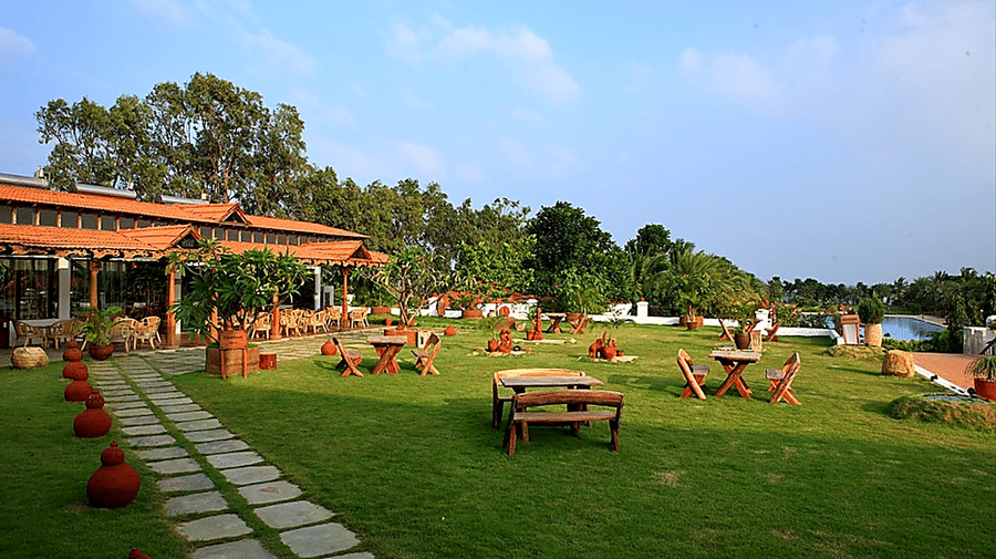Paanam - The Bar garden area with wooden picnic tables, a pathway, and pool views, set against a scenic resort backdrop