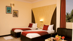 The Club Room at the best resort in Bangalore, with twin beds, a sofa, a table, and framed pictures | Ramanashree California Resort