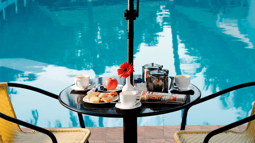 A poolside table with chairs, cups, plates, and food at the best resort in Bangalore | Ramanashree California Resort