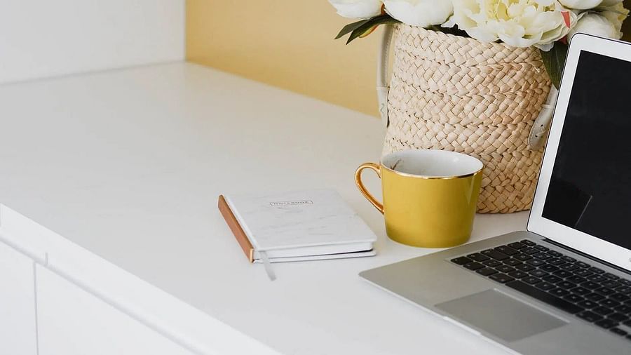 Clean, workspace with a laptop, notebook, mug, and flowers in a woven basket. 