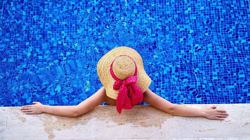 a woman wearing a jute hat chilling at the pool deck while her 3/4th of the body is dipped in the swimming pool