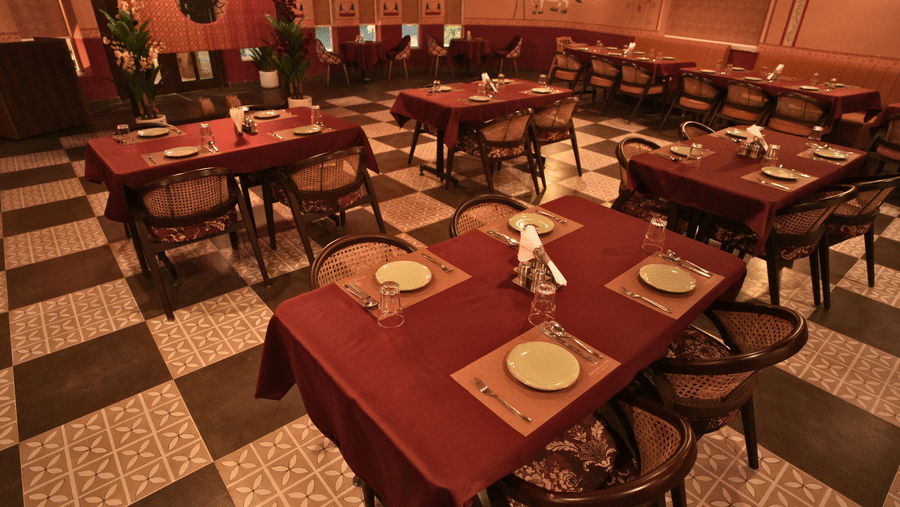Closeup of a warm, dimly lit restaurant interior featuring several tables covered in red tablecloths and a black and white checkered floor at Kadamb Kuteer, Vrindavan.