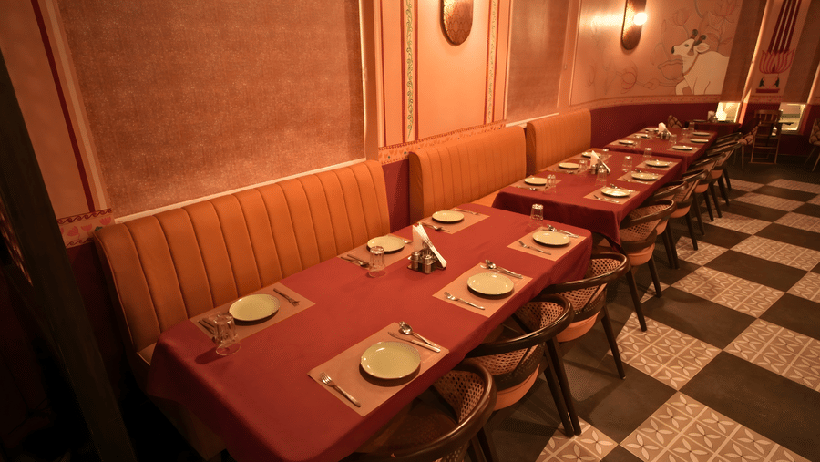 Interior view of Ekam restaurant at Kadamb Kuteer Vrindavan with booth seating, red tablecloths, wood paneling, and a checkered floor.