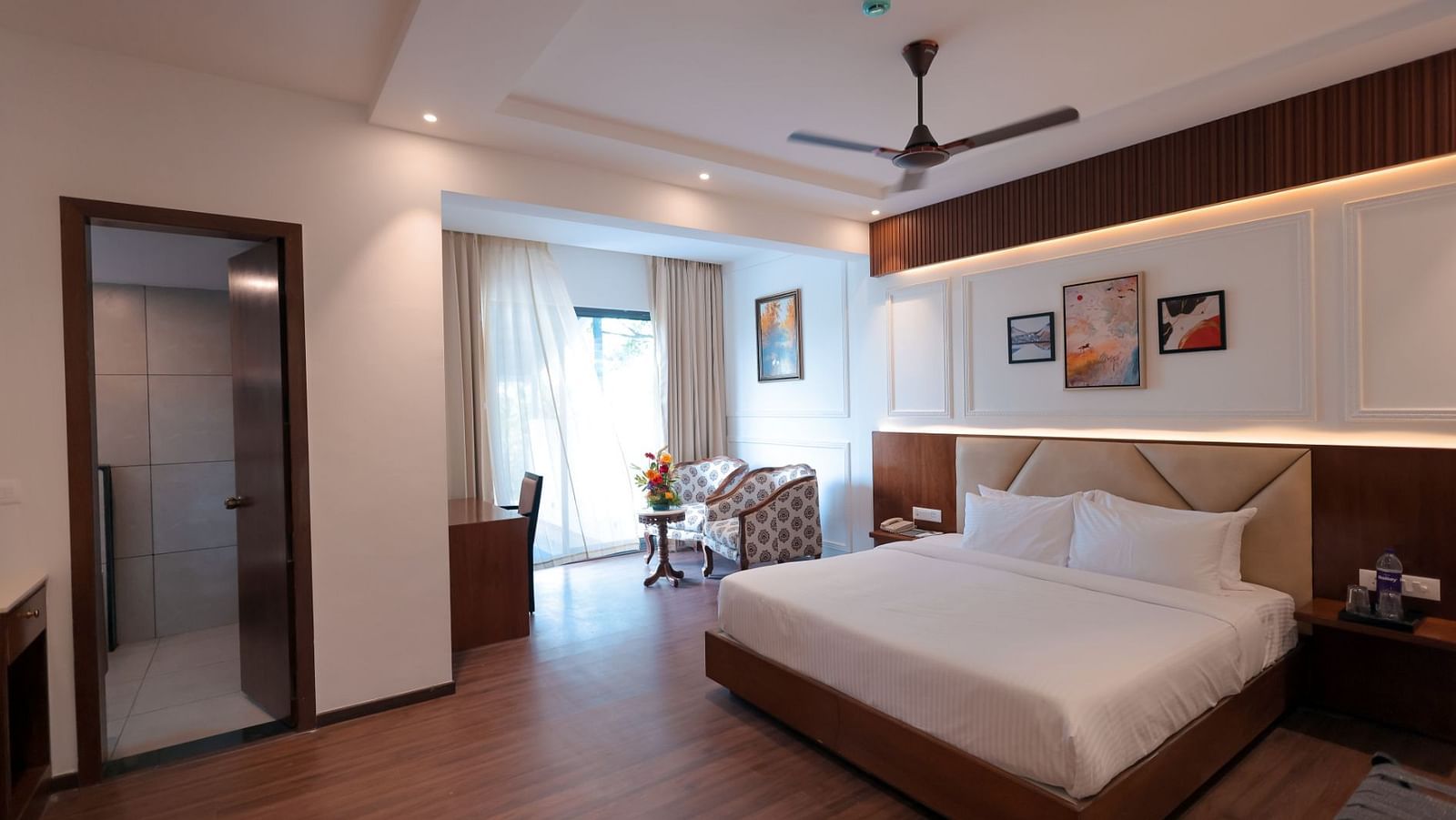 A room with double bed, framed wall art, fan, round table with chairs at A room with double bed, framed wall art , round table with two chairs at side at A bedroom with two single cot, fan and warm lights at Trishvam Symphony, Krishnagiri.