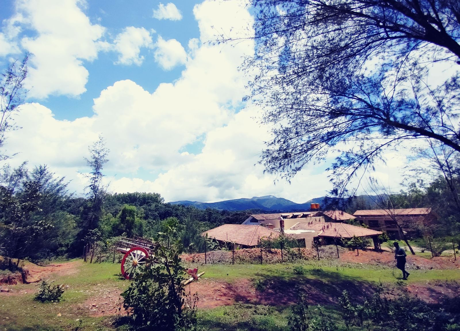 Landscape view of houses with tiled roofs amidst trees and greenery under a partly cloudy sky at Paradise Wild Hills Resort, Kollur.